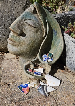 Stoneware sculpture of a head, with pieces of broken crockery sitting in the hair area