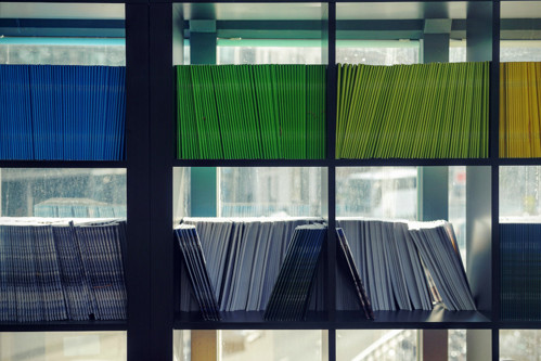 A bookshelf with many papers neatly arranged in blues, greens and yellows