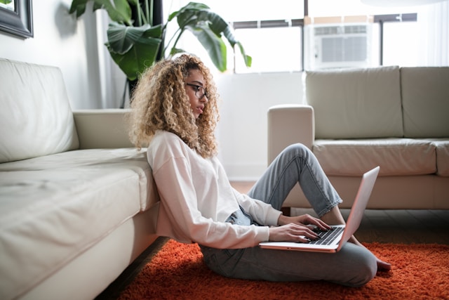 Profile image of woman sitting on the floor with a laptop on her leg, looking at the screen and typing