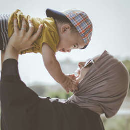 Mother in hijab and wearing sunglasses holding her child up while the small child grins down at her holding her face.