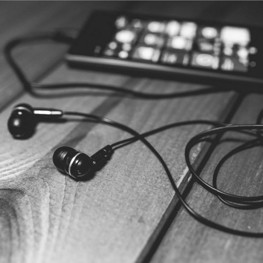 Black and white picture of earbuds connected by wire to a mobile phone in the background