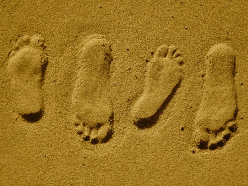 two sets of footprints in sand, suggesting a couple are standing close to each other, maybe hugging